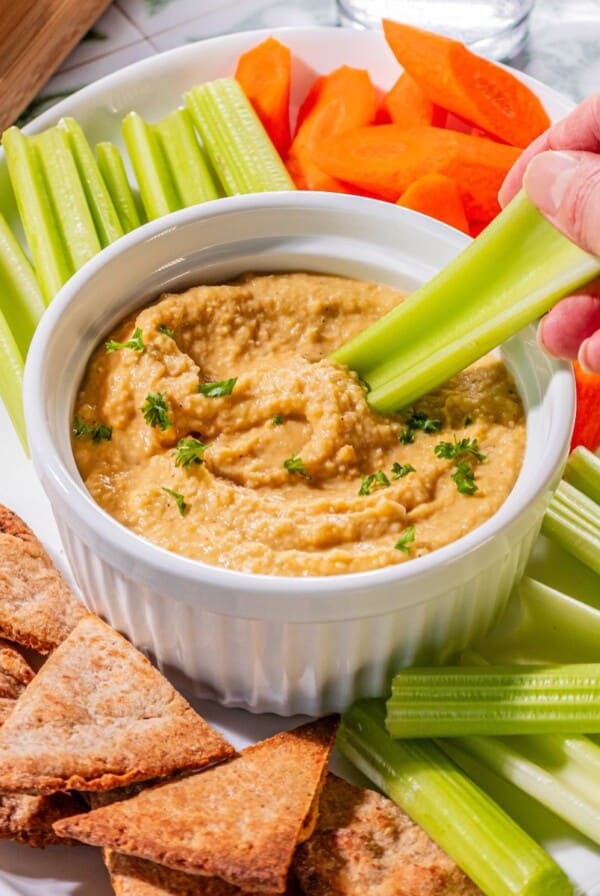 Garlic hummus being scooped up with a celery.