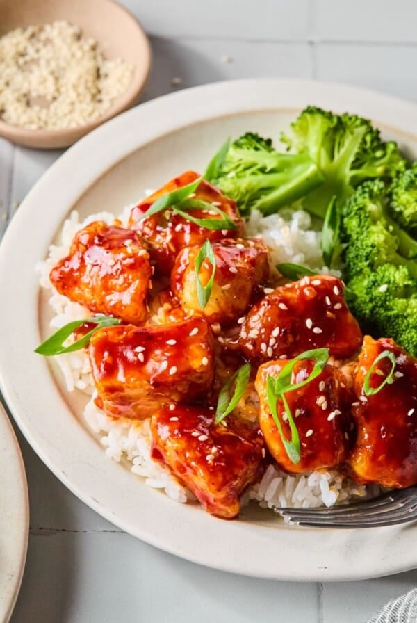 A plate with general tso chicken over rice and a side of broccoli.