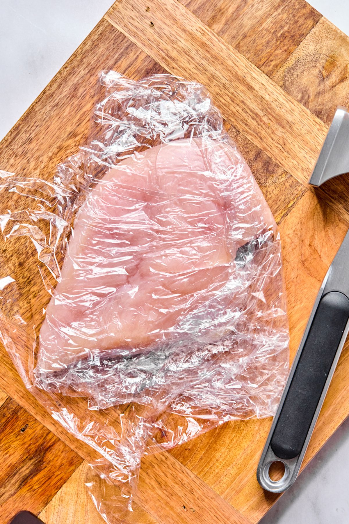 Raw chicken on a cutting board to be pounded flat.