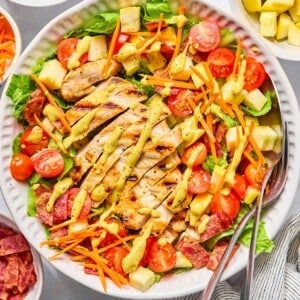 BLT chicken salad with dressing on top and utensils on the side.