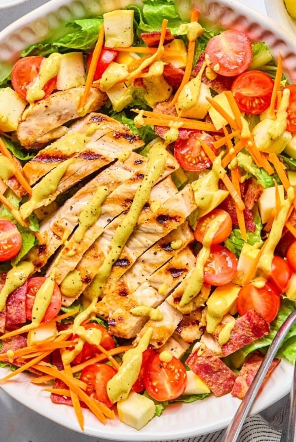 BLT chicken salad with dressing on top and utensils on the side.