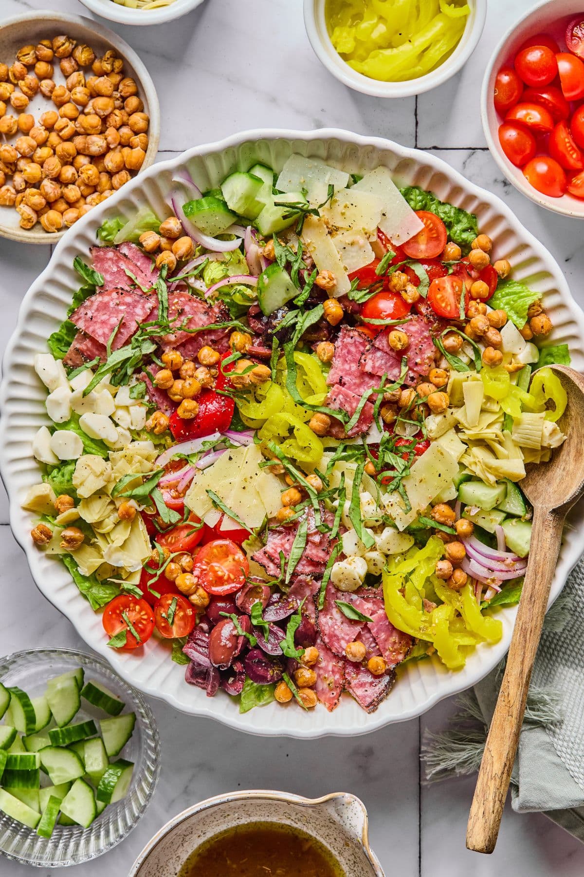 A bowl filled with chopped antipasto salad surrounded by bowls of ingredients.