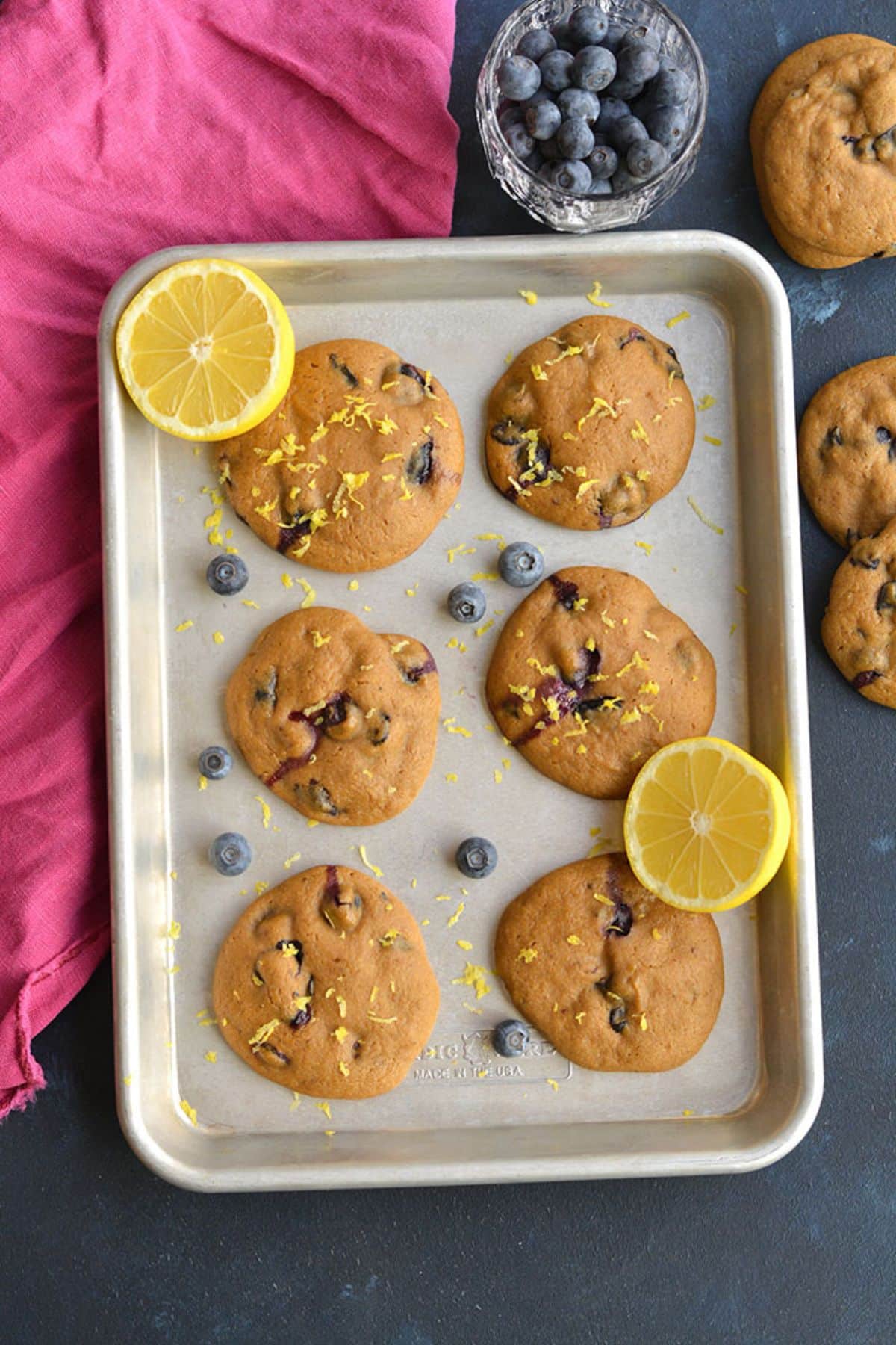 Healthy blueberry cookies on a baking sheet with fresh berries and lemon slices.