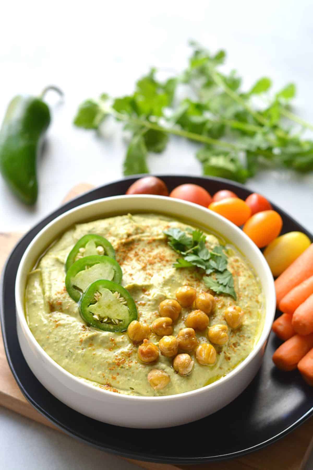 Jalapeno hummus in a bowl with veggies on the side.