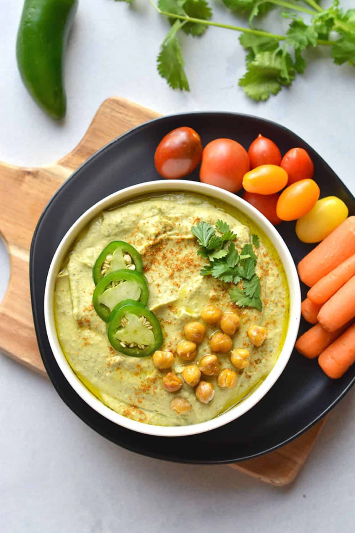 A plate of vegatables next to a bowl of jalapeno hummus.