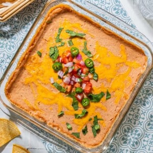 Pinto bean dip on a table and topped with salsa, jalapeno and cilantro.