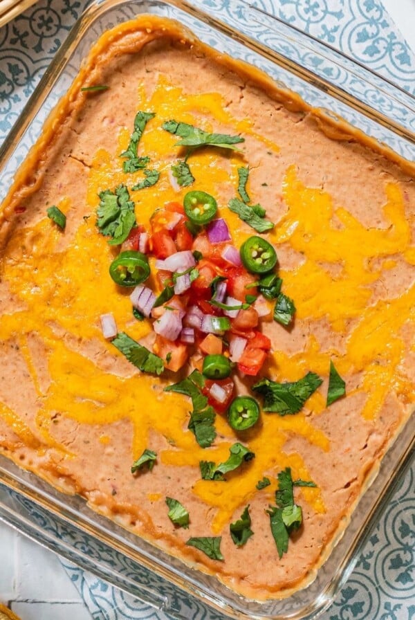 Pinto bean dip on a table and topped with salsa, jalapeno and cilantro.