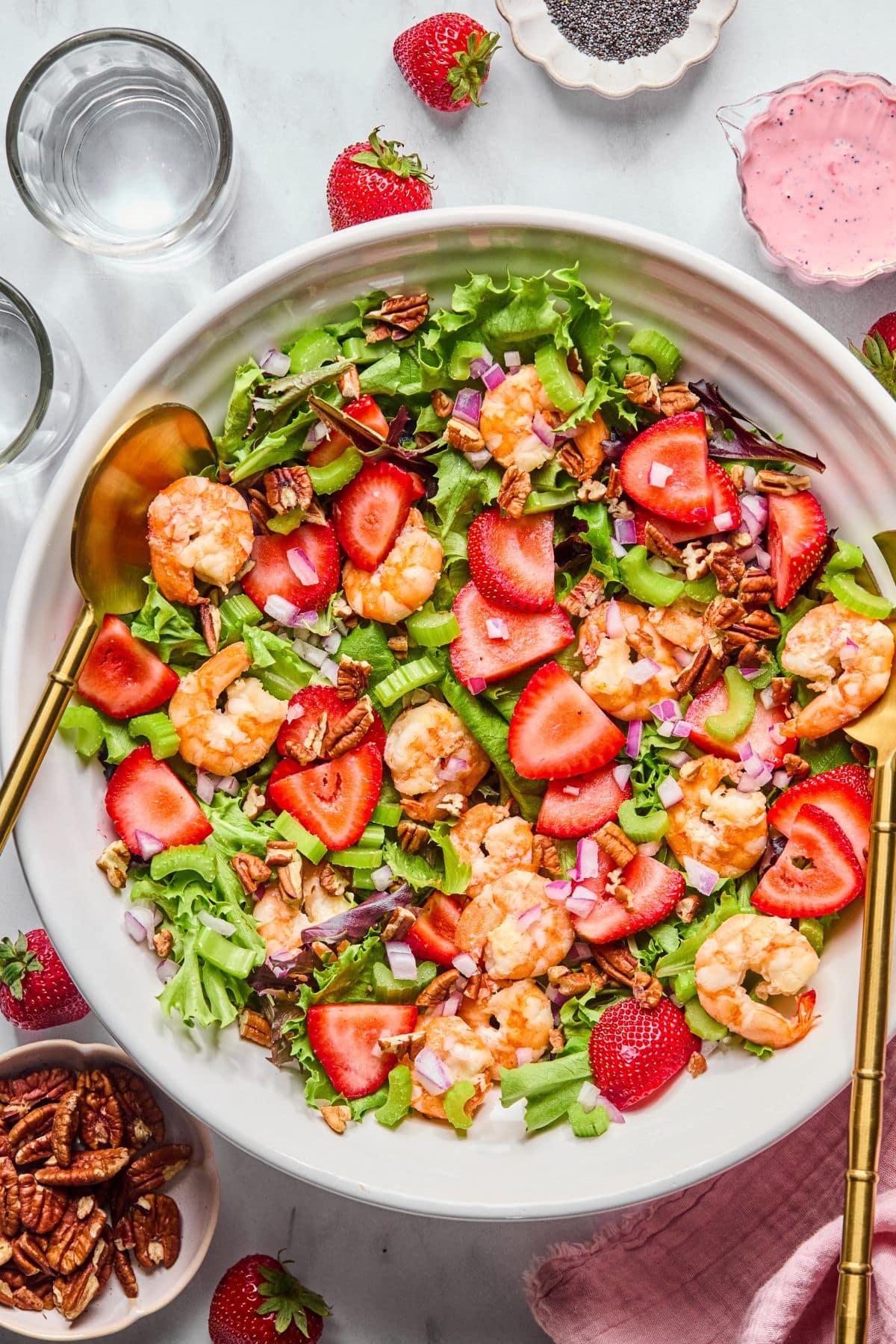 Add the mixed greens, chopped celery, chopped red onion, cooked shrimp, sliced strawberries and chopped pecans to a large bowl.