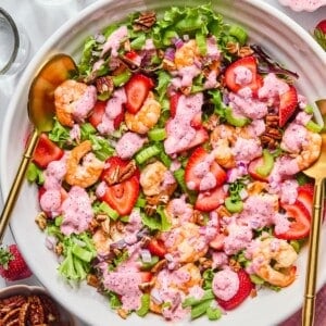 A bowl filled with strawberry shrimp salad with spoons on the side.