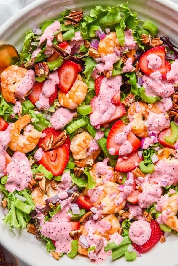 A bowl filled with strawberry shrimp salad with spoons on the side.