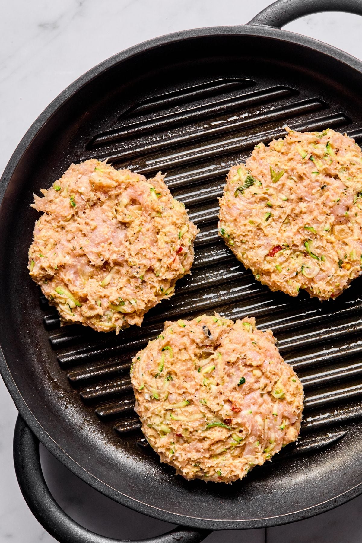 The burgers added to a skillet to cook.