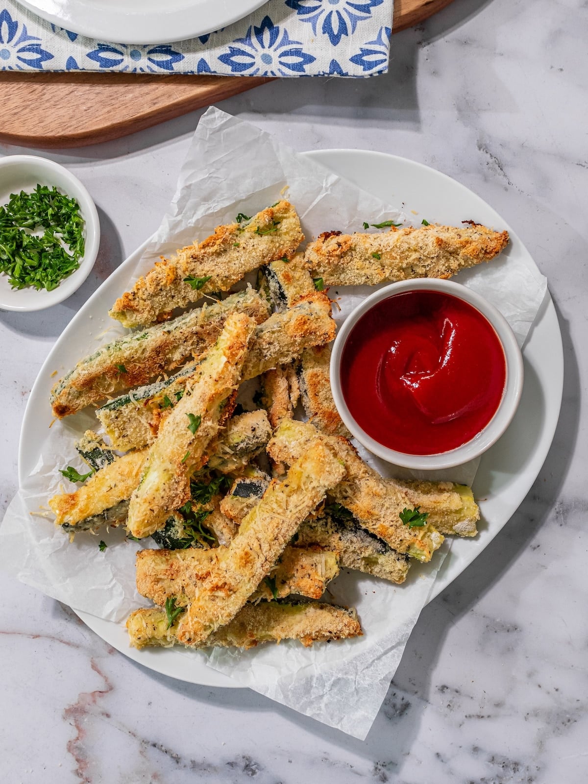 Baked gluten-free zucchini sticks on a platter with a dish of ketchup.