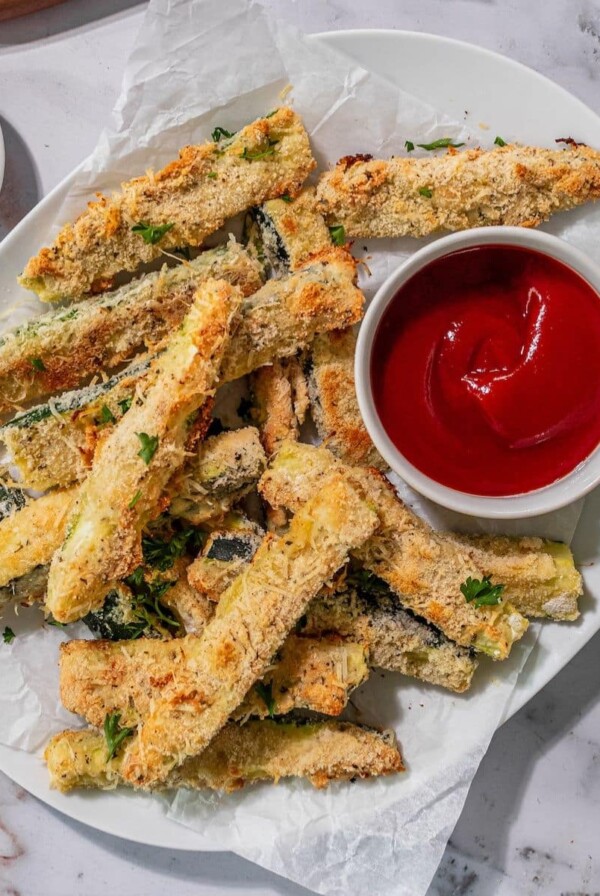 Baked zucchini sticks on a plate with ketchup on the side.