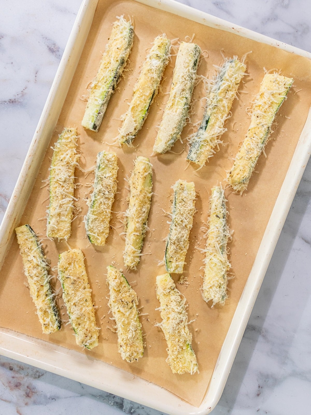 Breaded zucchini sticks on a baking tray lined with parchment.