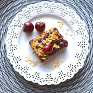 Cherry oatmeal bar piece on a plate with fresh berries and oats on the side.
