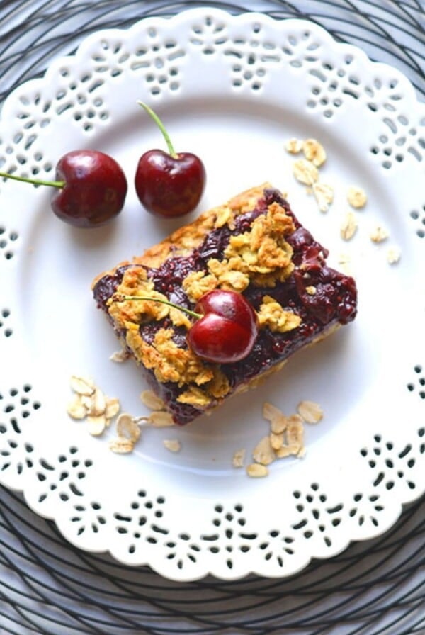 Cherry oatmeal bar piece on a plate with fresh berries and oats on the side.