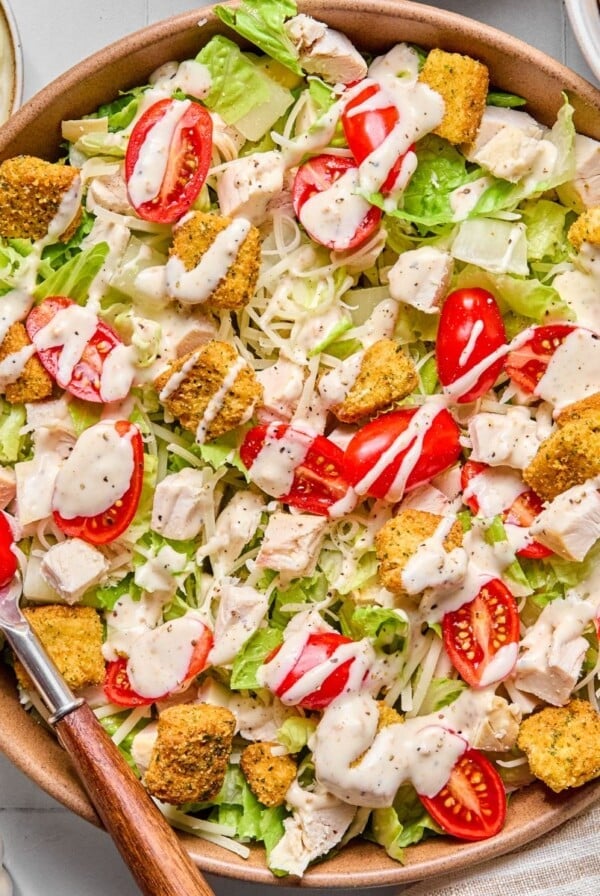 Healthy caesar salad with dressing on top and a fork on the side.