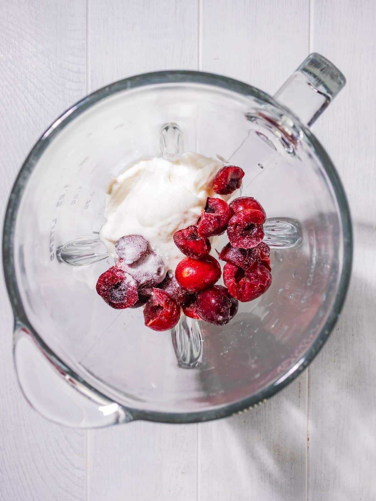 All ingredients to make a cherry smoothie in a blender.
