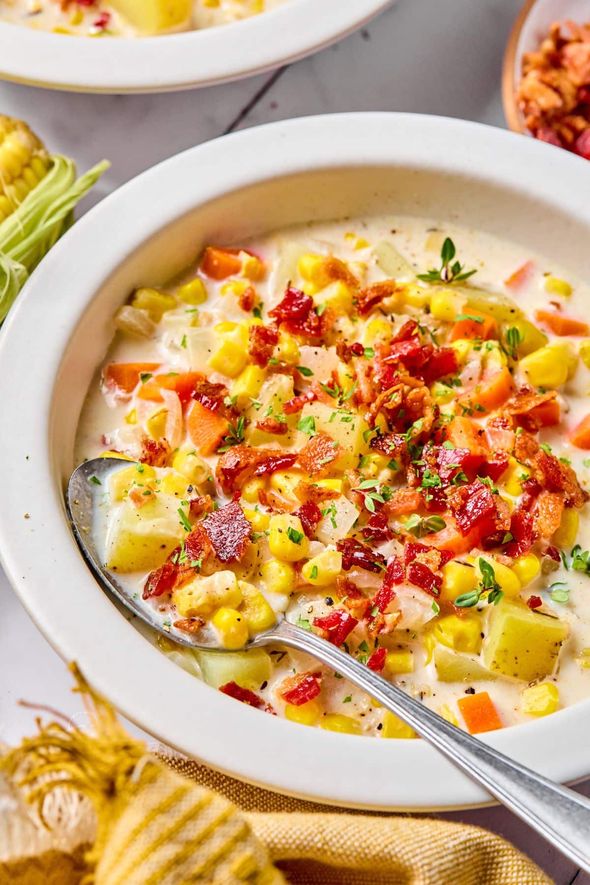 Corn chowder with bacon on top in a white bowl.