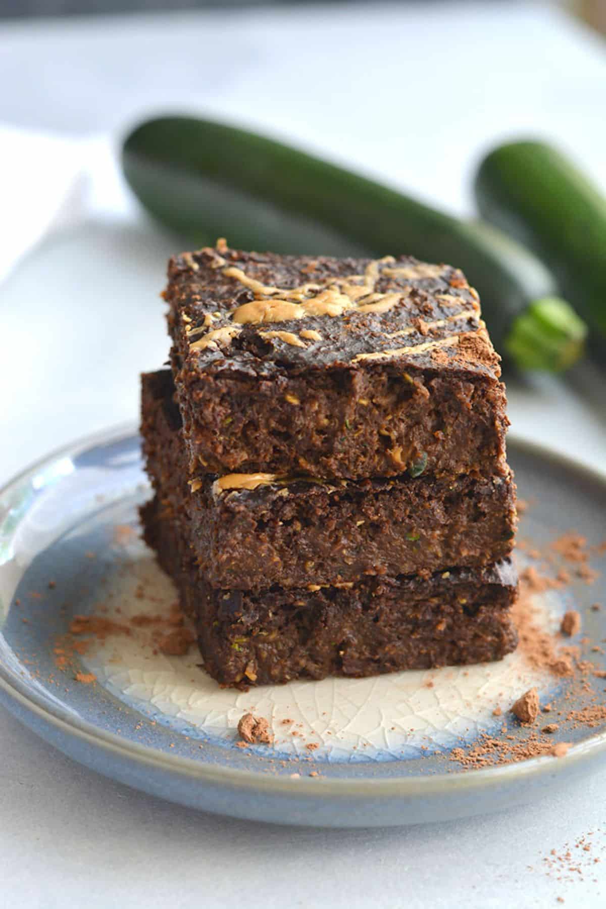 Healthy zucchini brownies stacked on top of each other on a plate.