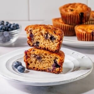 Sour cream blueberry muffins in half and stacked on a plate.