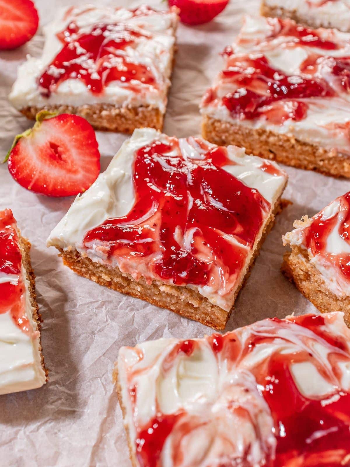 A bunch of cut up strawberry bars on parchment paper.