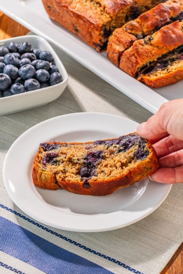 A slice of zucchini blueberry bread on a plate being picked up.