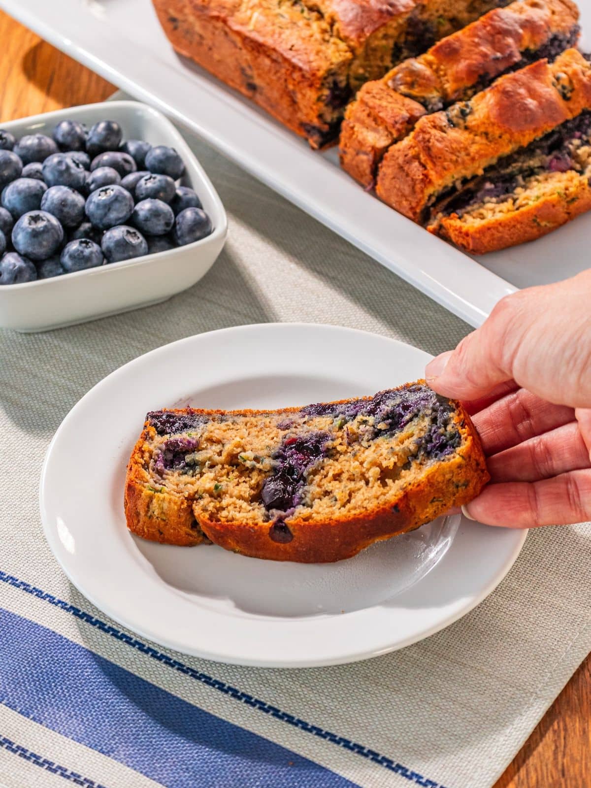 A slice of zucchini blueberry bread on a plate being picked up.