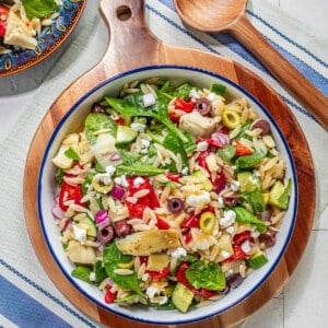 A bowl filled with a mediterranean salad with spinach, orzo, peppers and olives.
