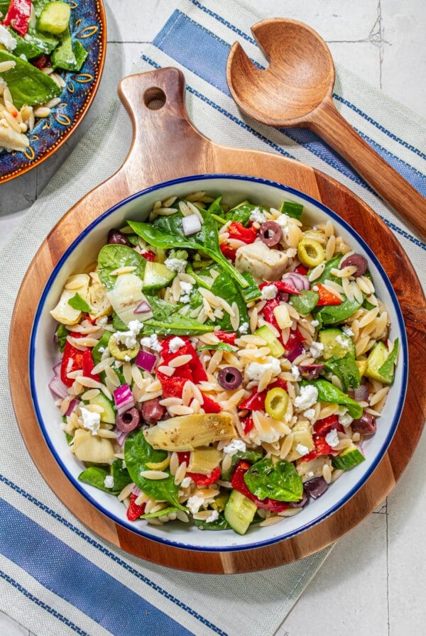 A bowl filled with a mediterranean salad with spinach, orzo, peppers and olives.