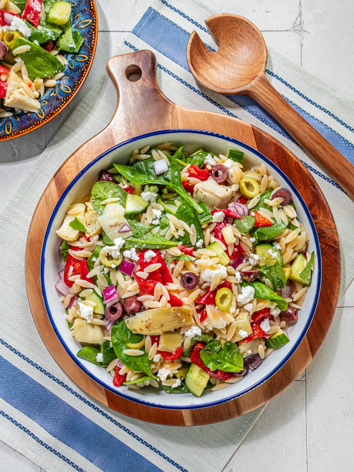 A bowl filled with a mediterranean salad with spinach, orzo, peppers and olives.