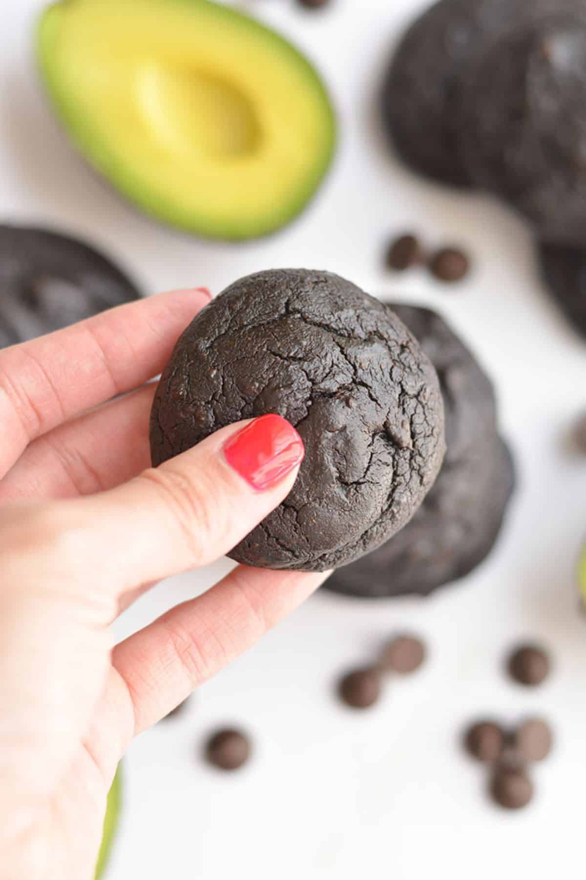 A hand holding up a chocolate avocado cookie in the air.