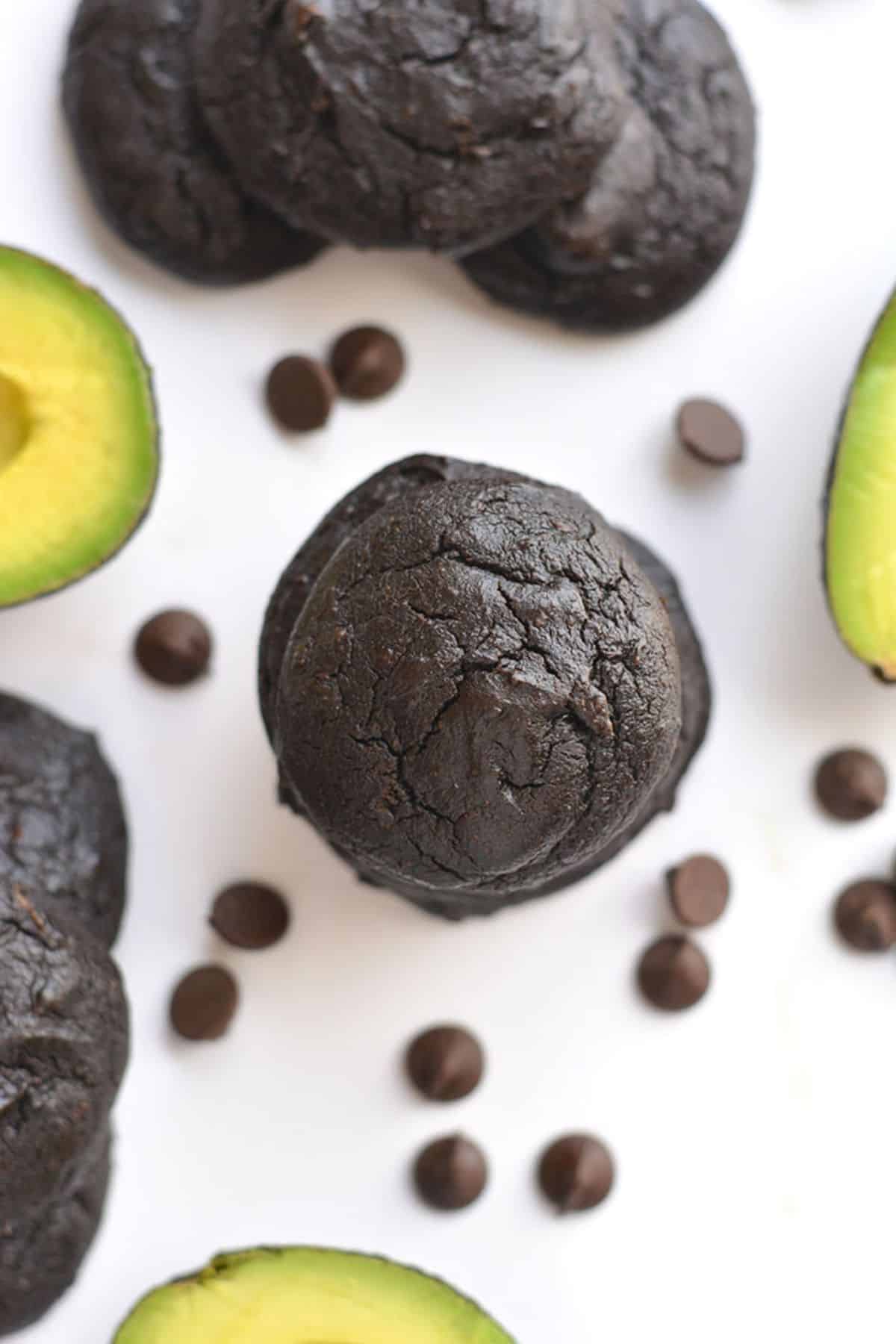 Avocado cookies all around a table with chocolate chips and avocado around the cookies.