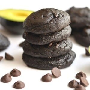 Avocado cookies with chocolate chips in the front, stacked on a table.