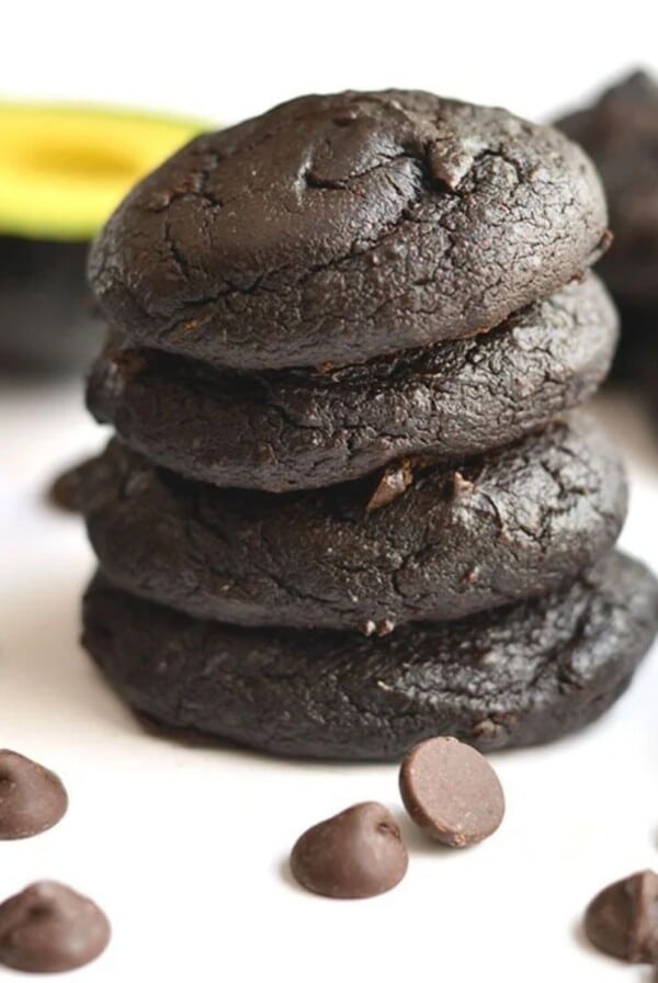 Avocado cookies with chocolate chips in the front, stacked on a table.