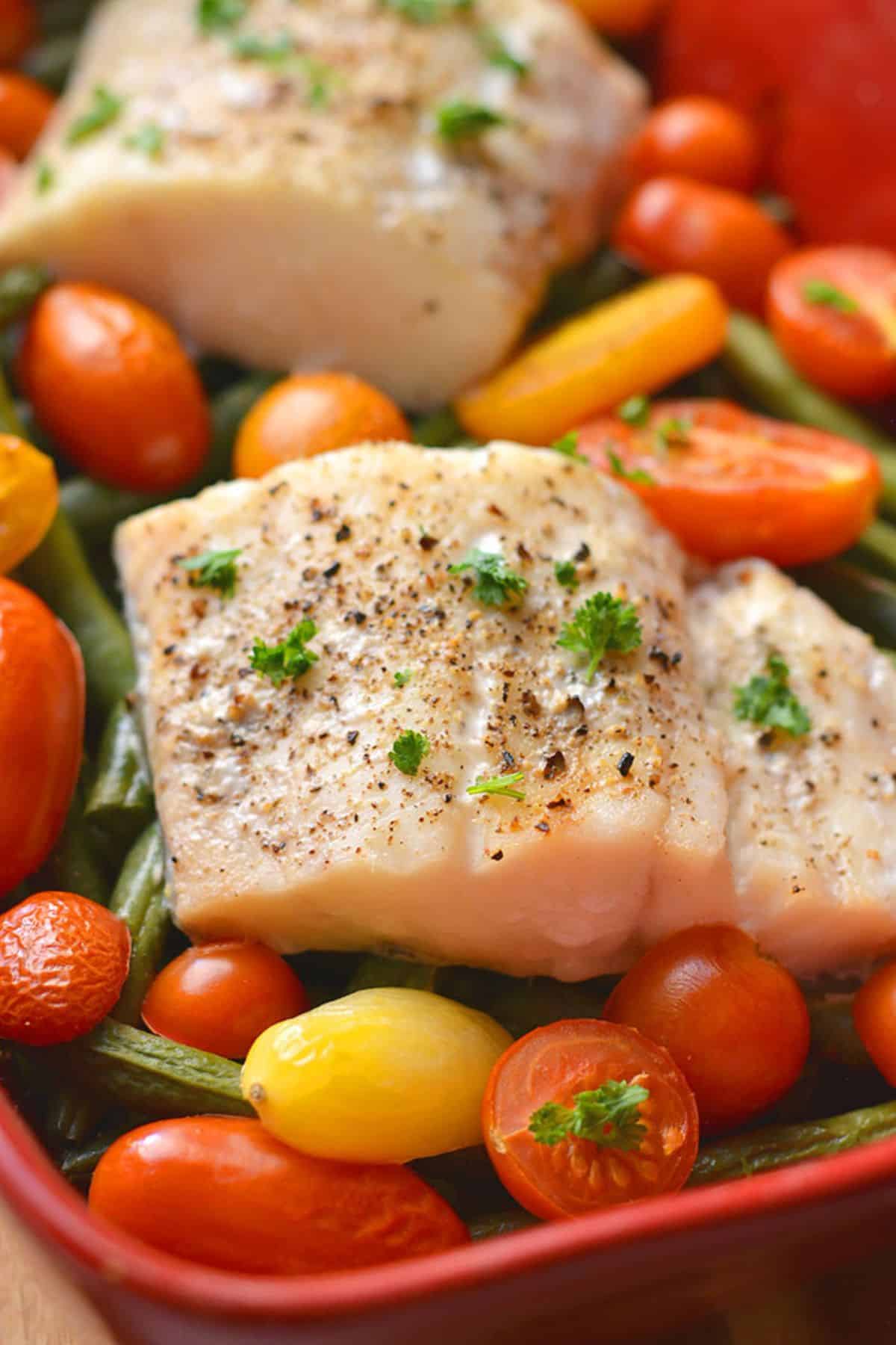 A piece of baked halibut over tomatoes and string beans.