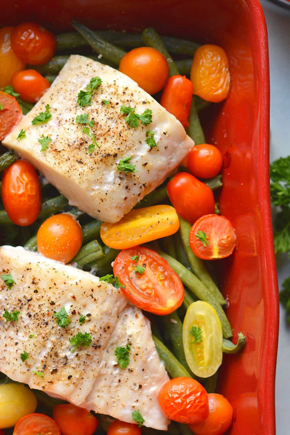 Pieces of baked halibut in a red baking dish over veggies.