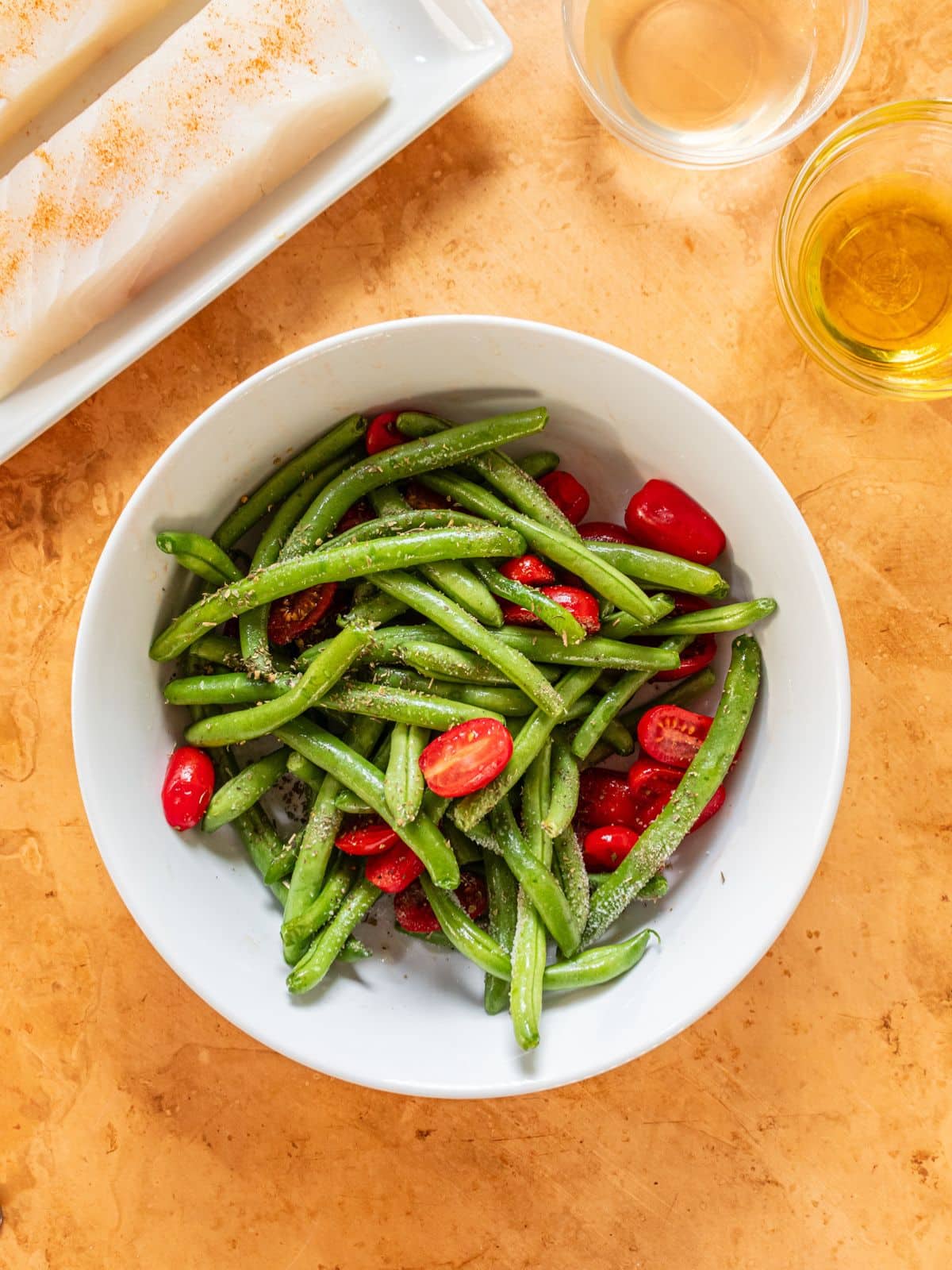 Green beans and tomatoes with seasoning in a bowl.