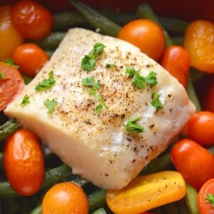 Baked halibut recipe on a sheet pan surrounded by veggies.
