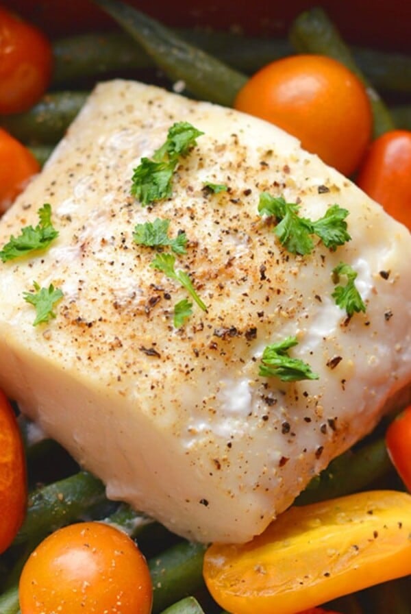 Baked halibut recipe on a sheet pan surrounded by veggies.