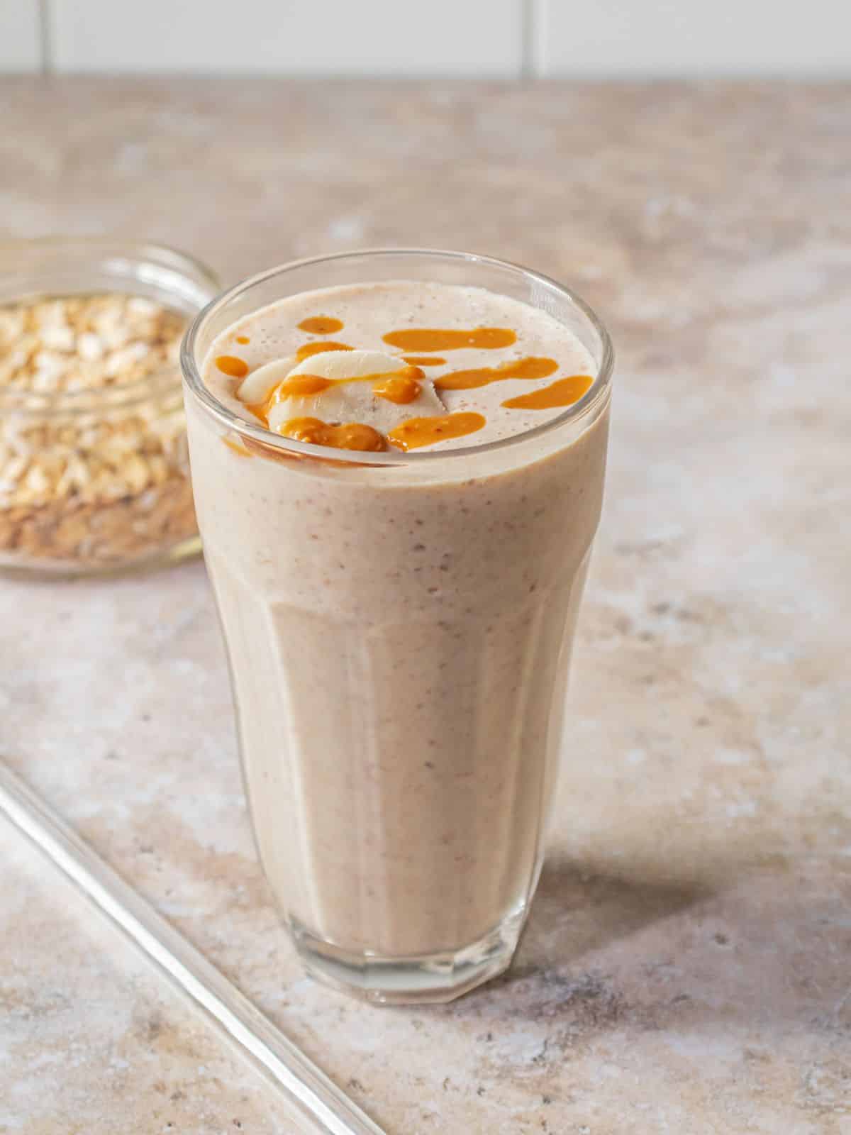 A glass full of a banana yogurt smoothie with banana and peanut butter on top.