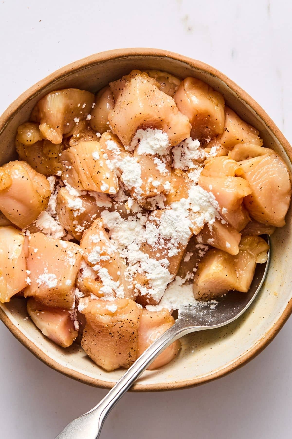 Chicken with spices and cornstarch in a bowl.