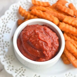 Homemade ketchup with tomato paste in a small cup next to sweet potato fries.