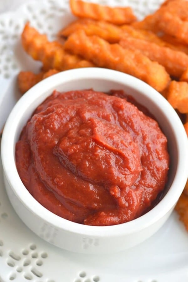 Homemade ketchup with tomato paste in a small cup next to sweet potato fries.
