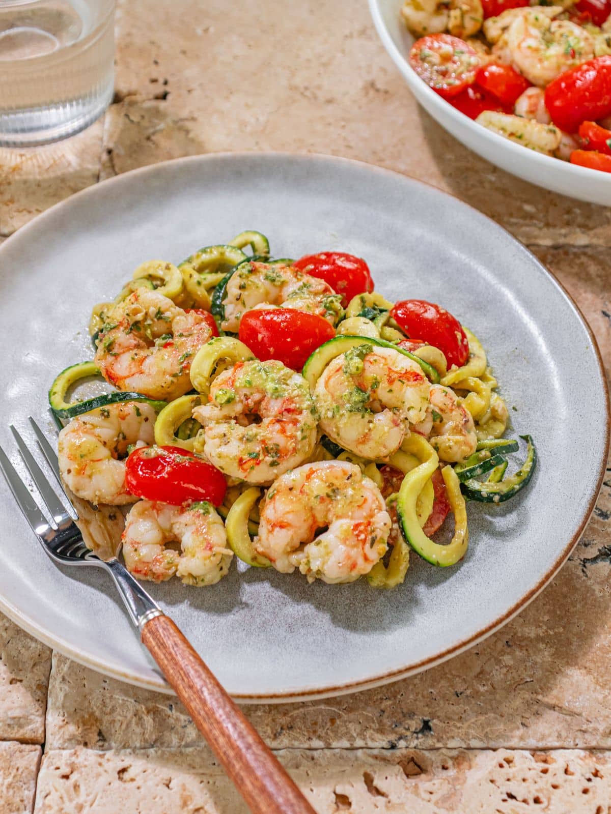 A plate of pesto shrimp and zucchini with a fork on the side.