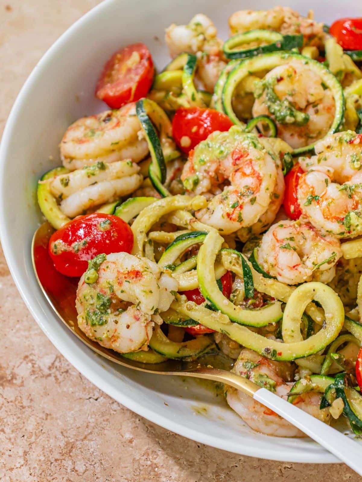 A spoon with a piece of pesto shrimp and tomato.