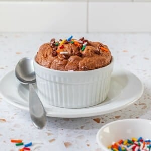 A single serve protein cookie in a white bowl with a spoon on the side.