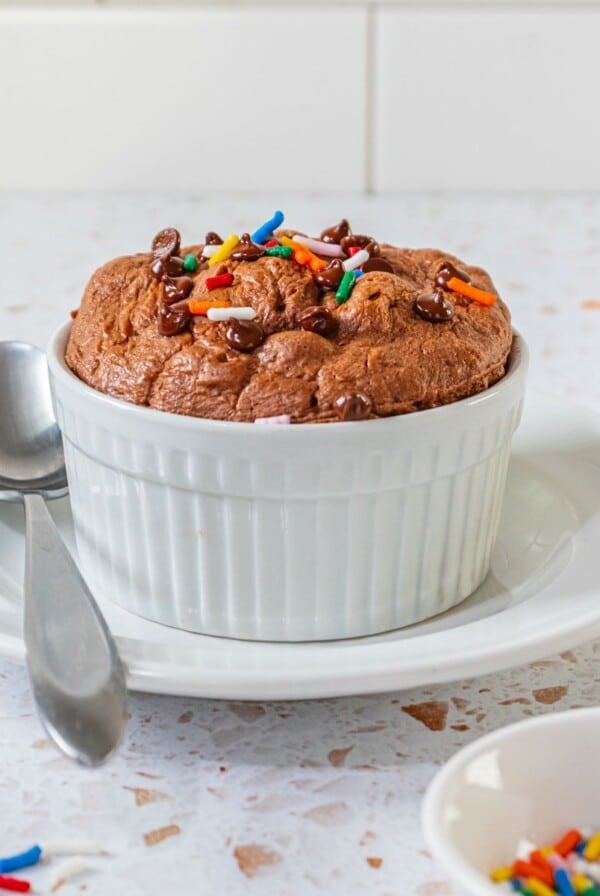 A single serve protein cookie in a white bowl with a spoon on the side.