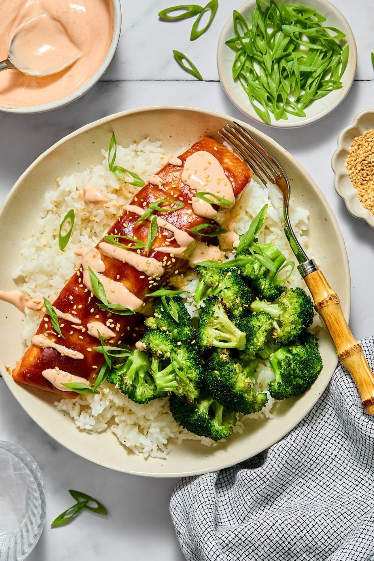 Baked teriyaki salmon over rice on a plate with broccoli and a sauce drizzled over the fish.