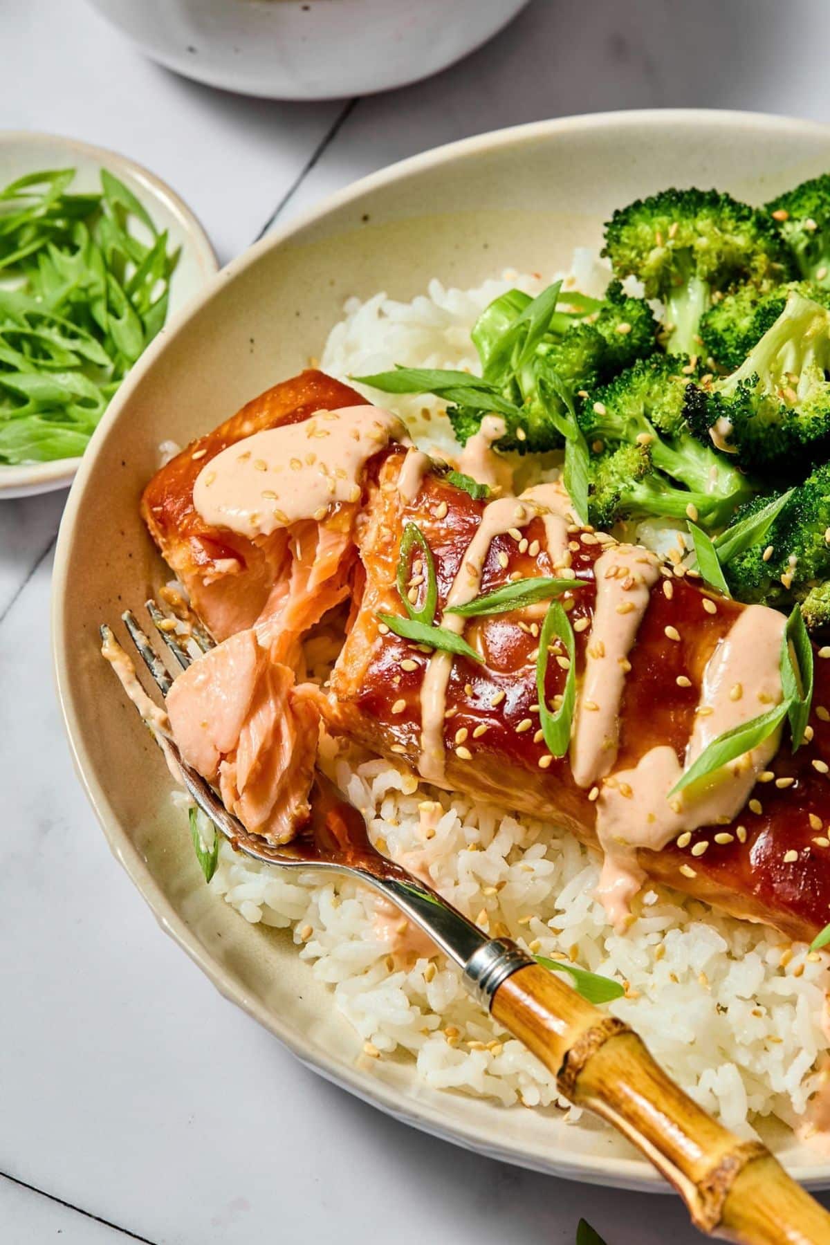 A fork holding a piece of baked teriyaki salmon from the plate.